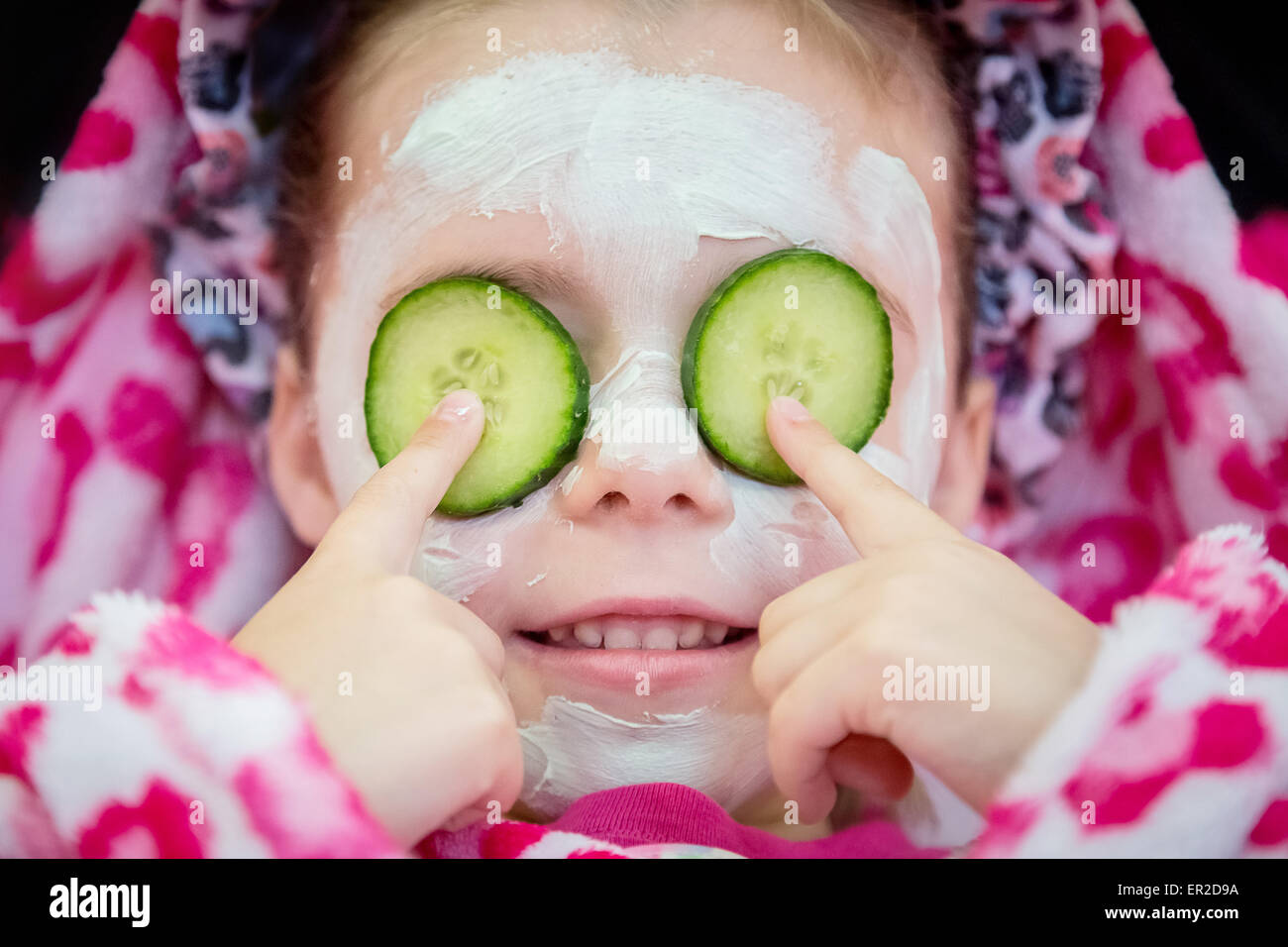 Young child relaxing with cucumber slices over eyes during a spa facial beauty treatment session Stock Photo