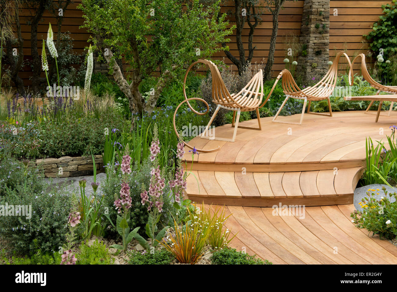 Curved wooden decking and chairs surrounded by borders in The Royal Bank of Canada Garden at The Chelsea Flower Show. Stock Photo