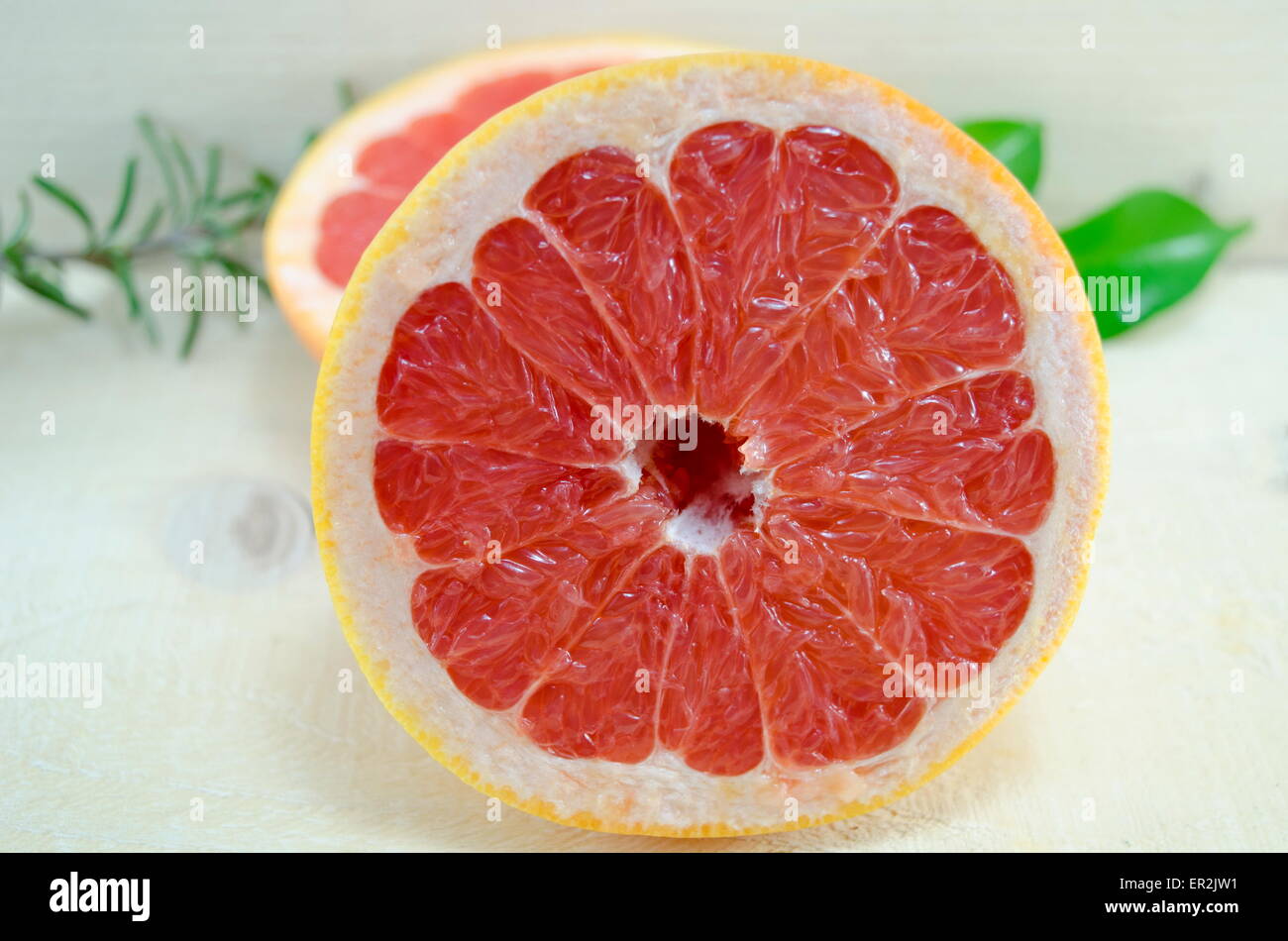 Fresh sliced grapefruit and rosemary branch on a wooden table Stock Photo