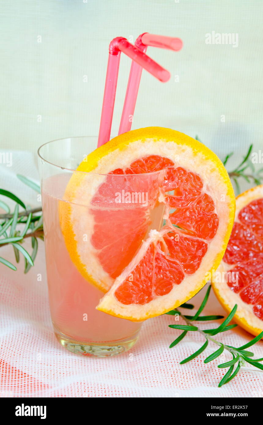 Fresh grapefruit juice in a glass decorated with red grapefruit slice on  a table decorated with rosemary branch Stock Photo