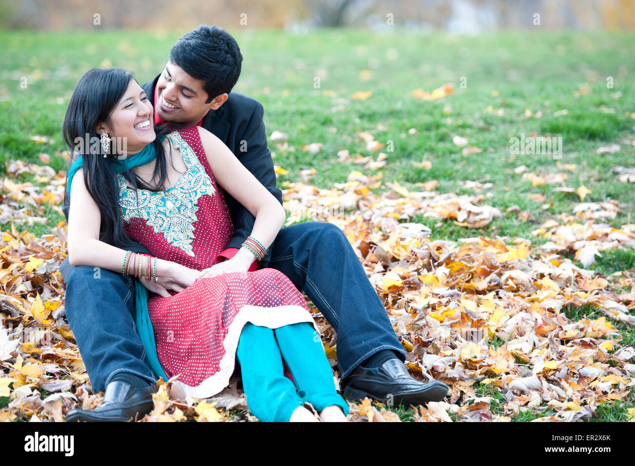 A young and happy Indian couple posing on a pile of leaves in the fall ...