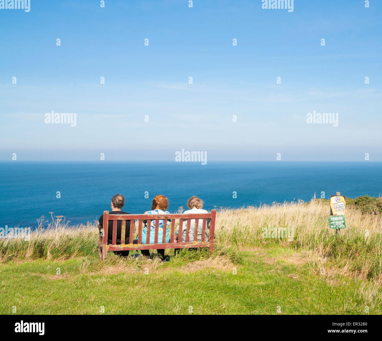 People sitting on bench overlooking sea on cliffs at Kettleness on the North Yorkshire coast near Whitby, England, UK Stock Photo