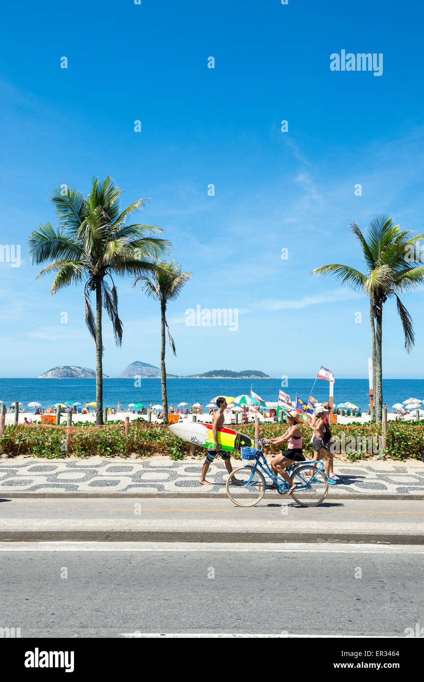 RIO DE JANEIRO, BRAZIL - MARCH 08, 2015: Brazilians walk and ride bicycles with surfboards on the beachfront boardwalk Ipanema. Stock Photo