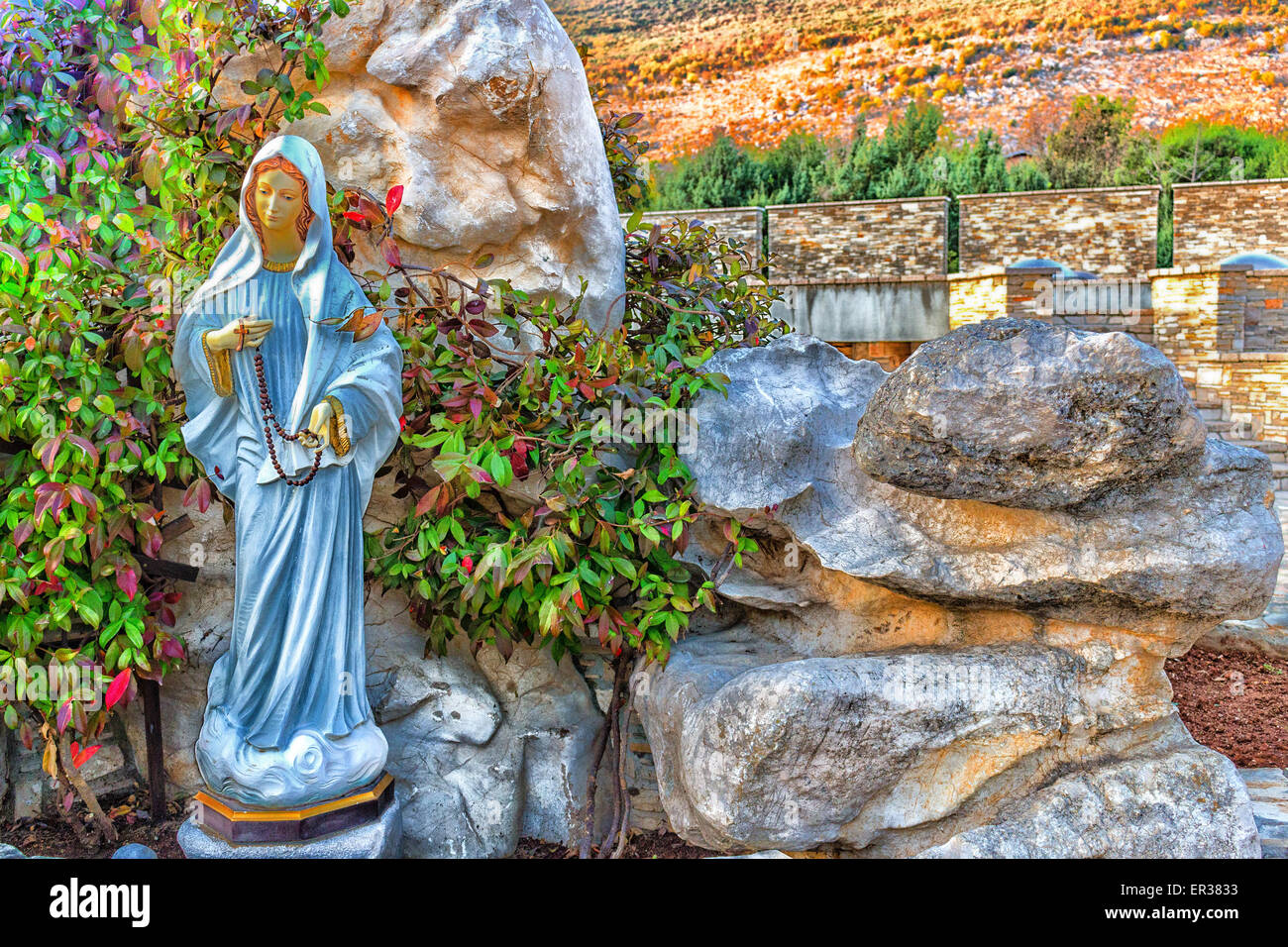Statue of the Blessed Virgin Mary with wooden prayer beads necklace in a house rock  garden  with treesin  Medjugorje Stock Photo