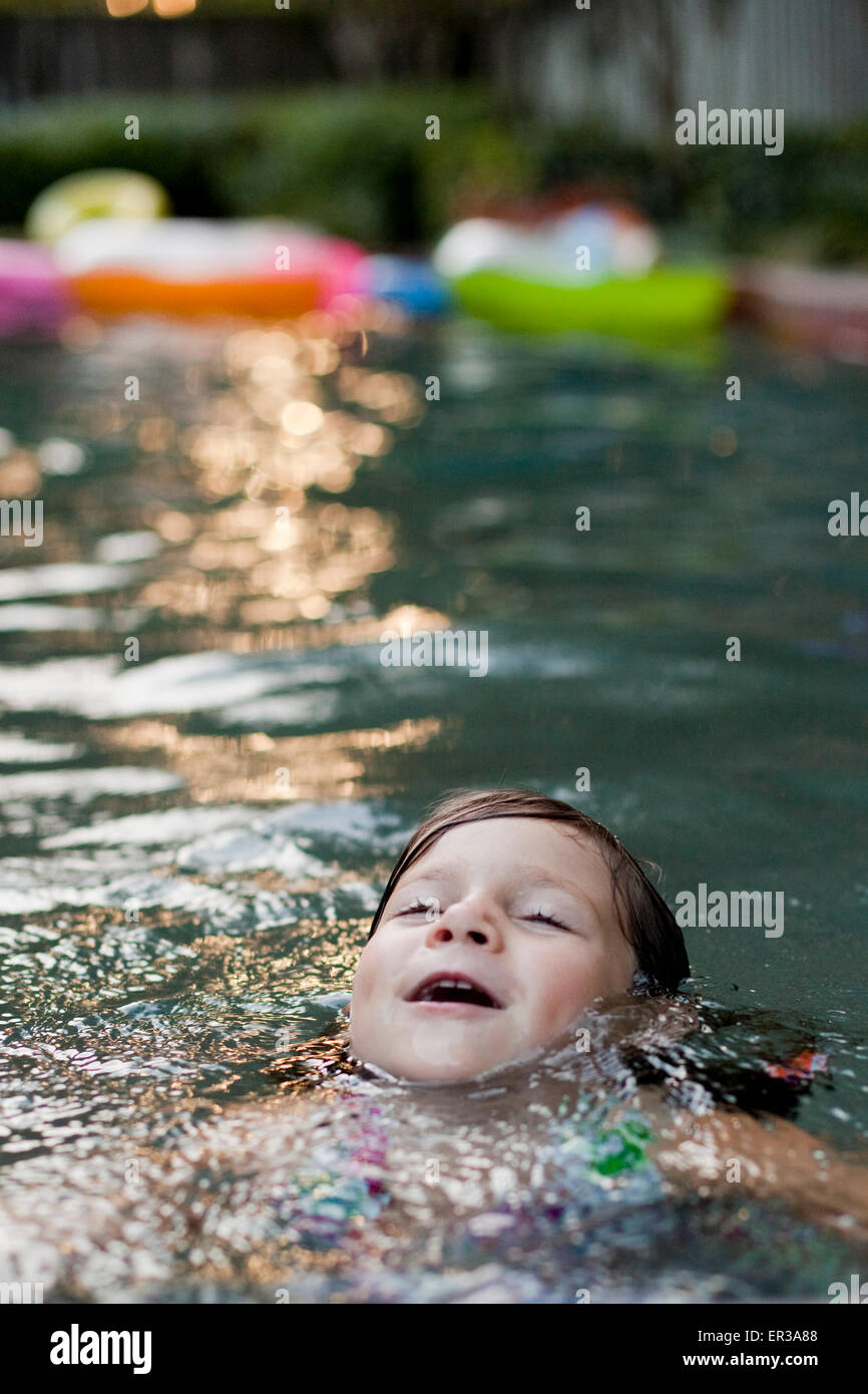 young girl floating in swimming pool with inner tubes and floaties in