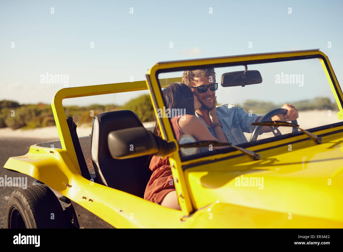 Woman kissing man driving car. Couple on road trip. Romantic caucasian couple on holiday having fun in car. Stock Photo