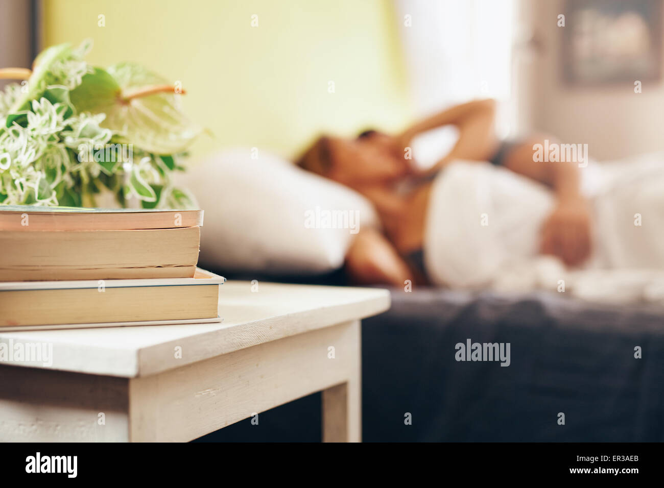 Side table with books and flowers by the bed in bedroom. Couple sleeping peacefully on bed. Stock Photo