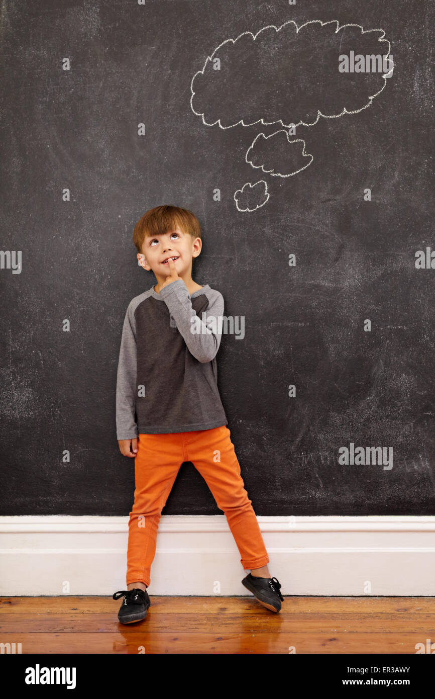 Child thinking with a thought bubble on the blackboard. Full length shot of cute little boy standing at home. Inspiration and so Stock Photo