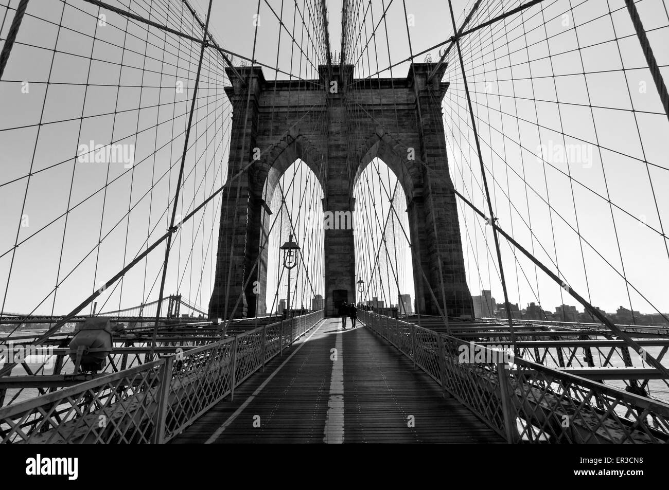 Silhouette of unknown people walking across the Brooklyn Bridge as the sun rises over the arches to the east - Black and White. Stock Photo