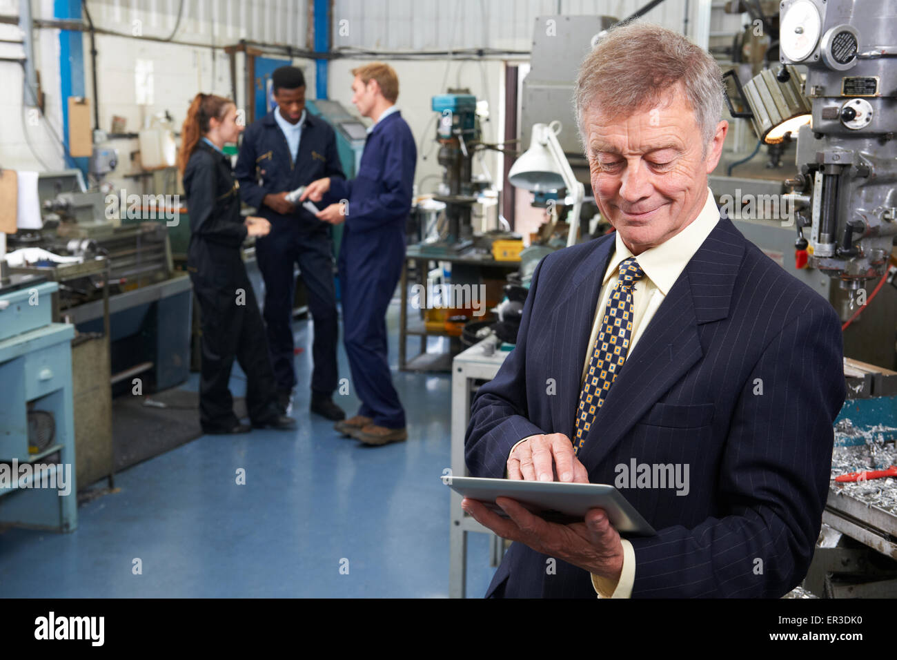 Owner Of Engineering Factory Using Digital Tablet With Staff In Background Stock Photo