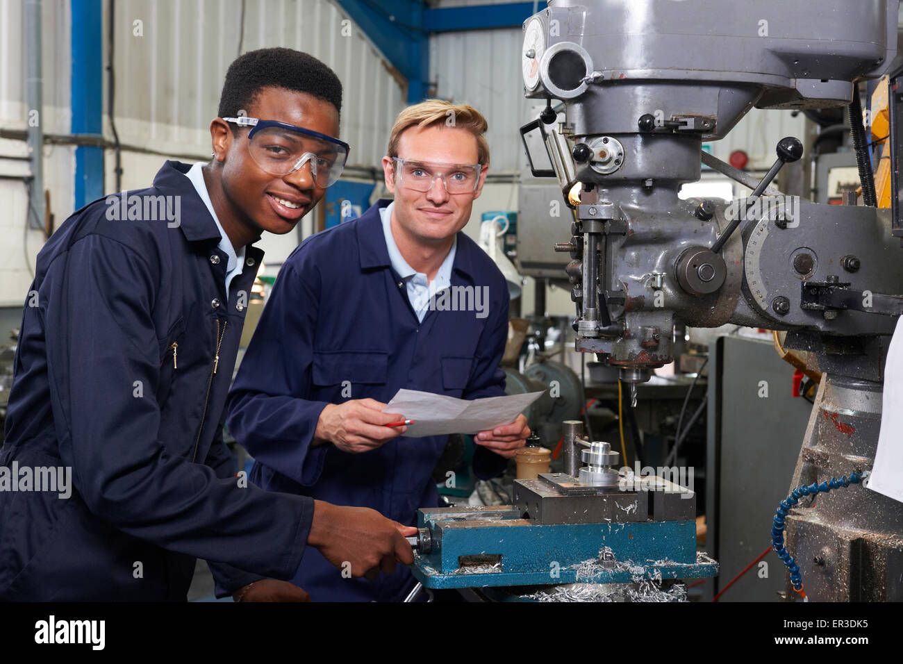 Engineer Showing Apprentice How to Use Drill In Factory Stock Photo