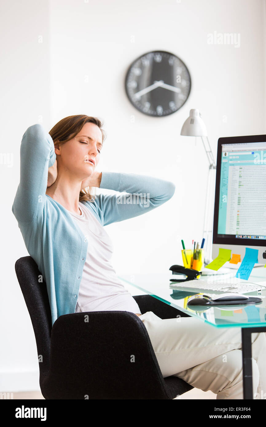 Woman suffering from neck pain in office. Stock Photo