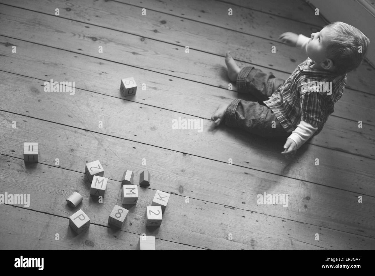 Baby boy sitting on nursery floor with wooden blocks Stock Photo