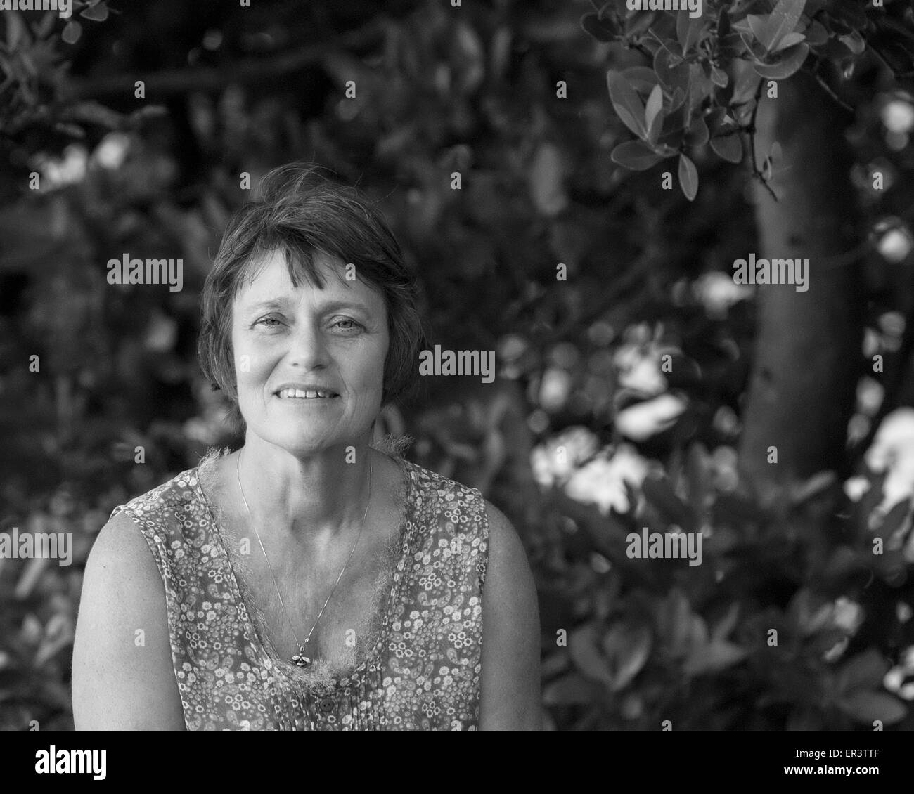 Senior woman sitting outside.  Looking at the camera.  Image is black and white.  Trees in the background. Stock Photo