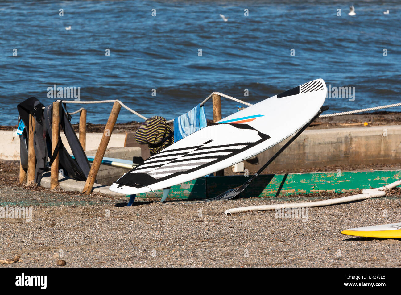 black and white surf board on rope near wetsuits in front of the sea
