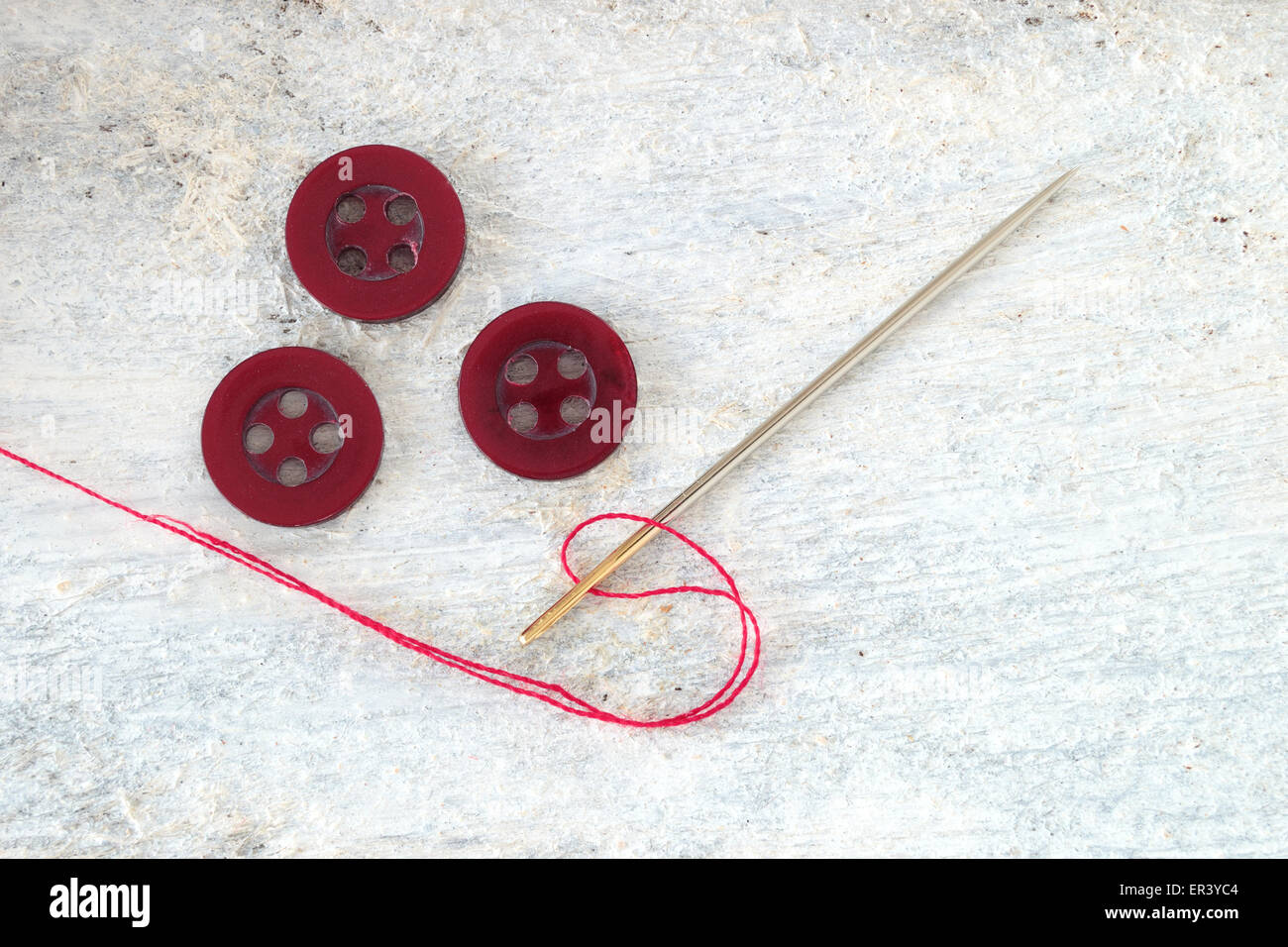 Sewing needle threaded with a red thread ready for sewing. Next , three