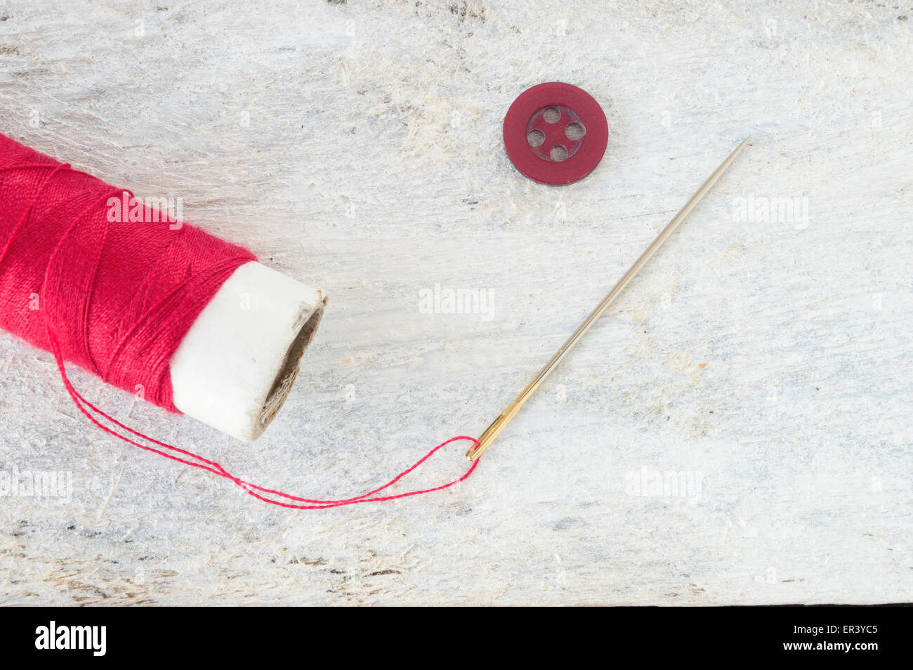 Sewing needle threaded with a red thread ready for sewing. Next , a