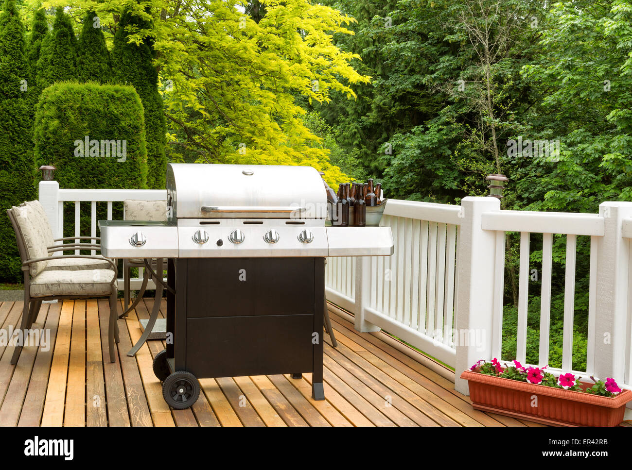 Photo of clean barbecue cooker with cold beer in bucket on cedar deck. Table and colorful trees in background. Stock Photo