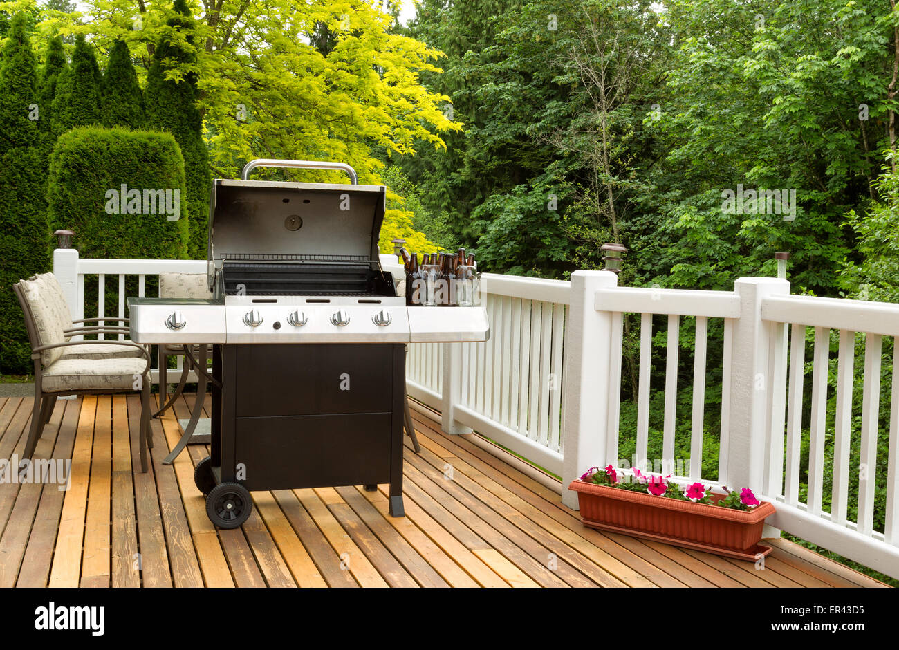 Photo of an open barbecue cooker with cold beer in bucket on cedar wooden patio. Table and colorful trees in background. Stock Photo