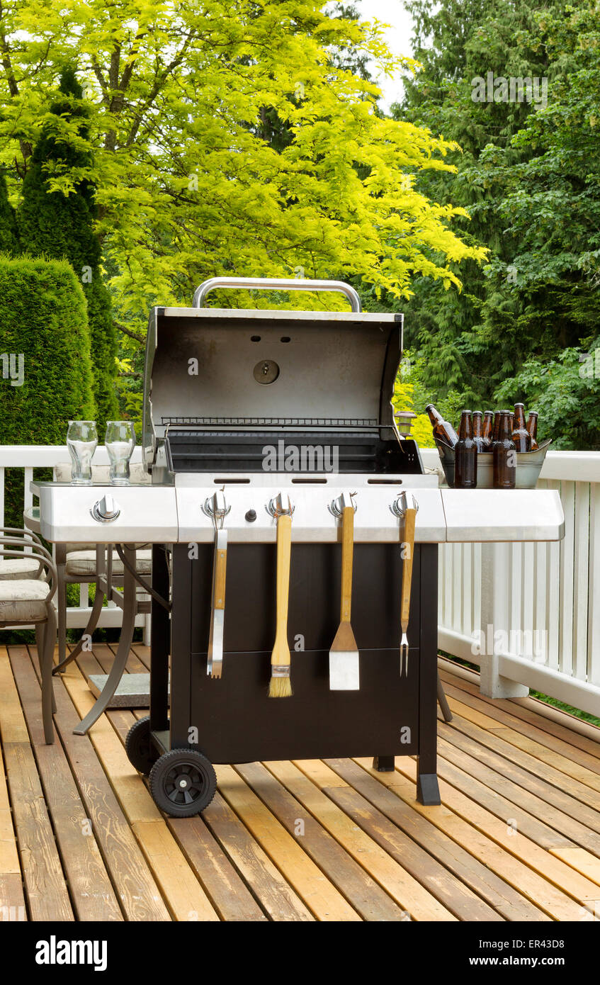 Vertical photo of an open barbecue cooker with cookware and cold beer in bucket on cedar wood patio. Table and colorful trees in Stock Photo