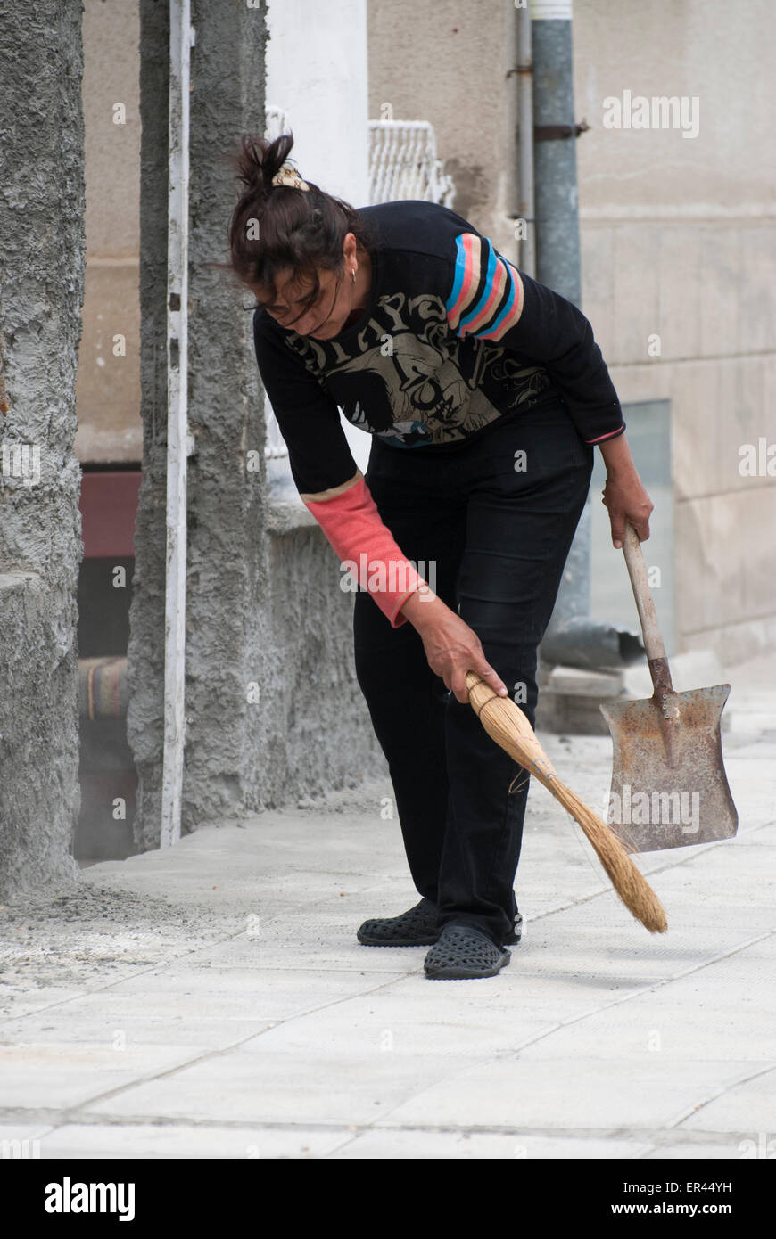 Woman working to sweep up a sidewalk Stock Photo