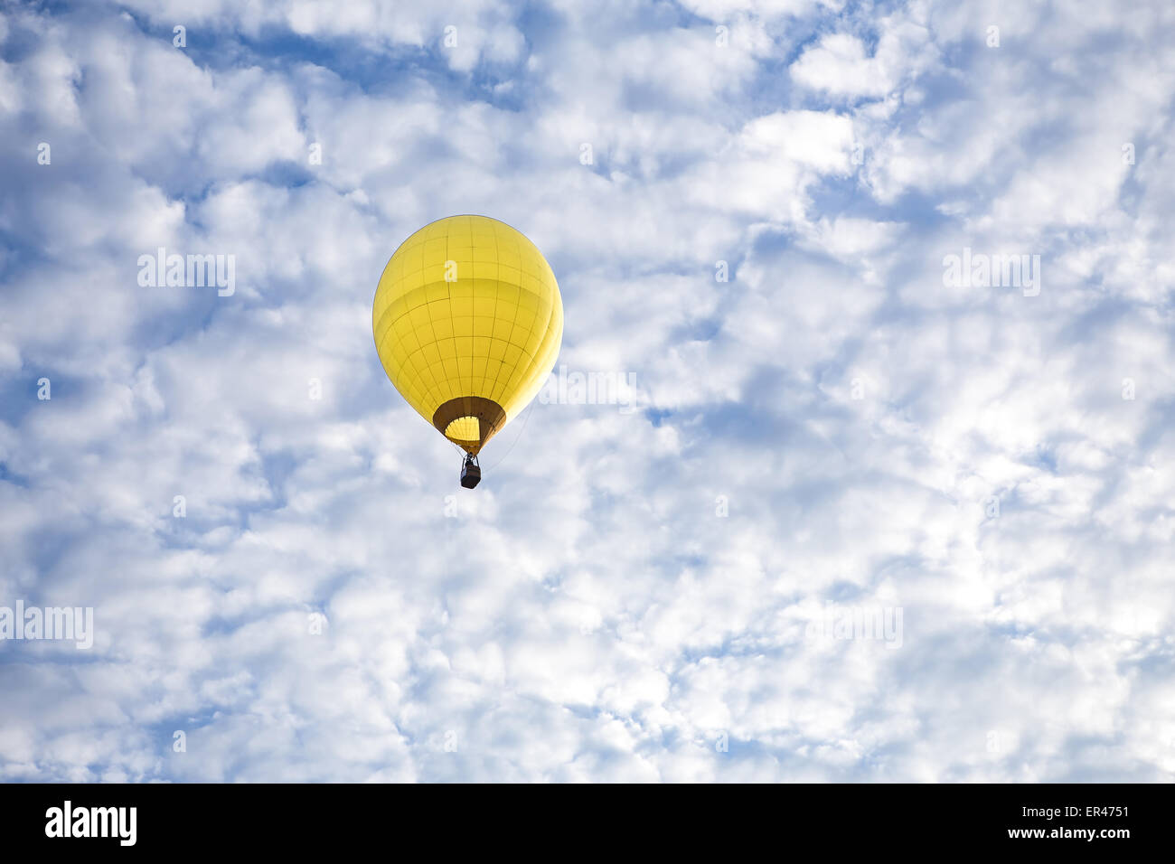 Yellow hot air balloon ascends into a blue sky with puffy white clouds, early in the morning. Stock Photo