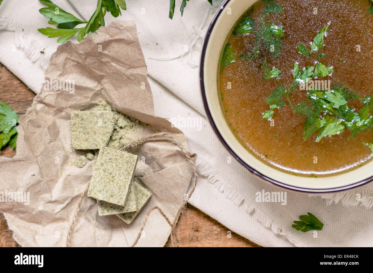 Bouillon cubes next to a bowl of broth. Parsley close, top view Stock