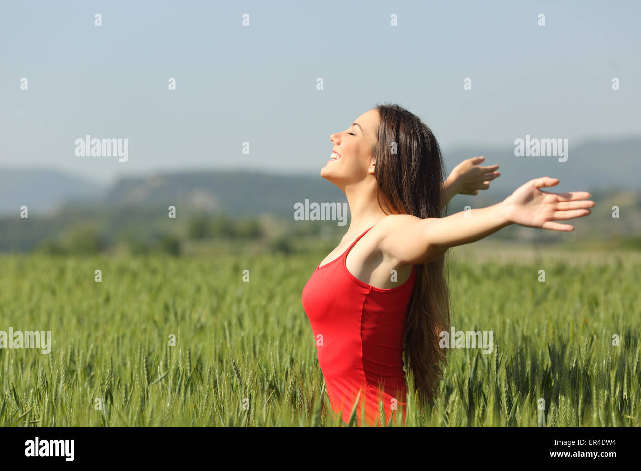 Woman breathing deep fresh air in a green wheat field wearing a red shirt Stock Photo