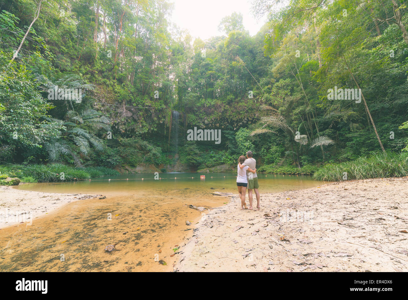 Couple watching a stunning multicolored natural pool and waterfall in the rainforest of Lambir Hills National Park, Borneo. Stock Photo