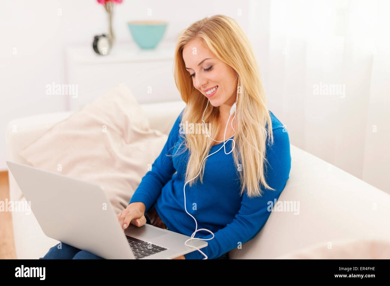 Smiling woman sitting on sofa with headphone and laptop Stock Photo - Alamy