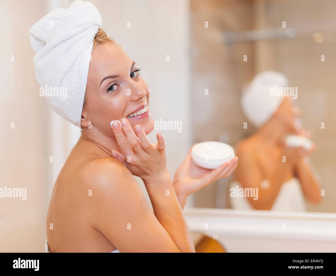 Happy woman applying moisturizer on face after the shower. Debica, Poland Stock Photo