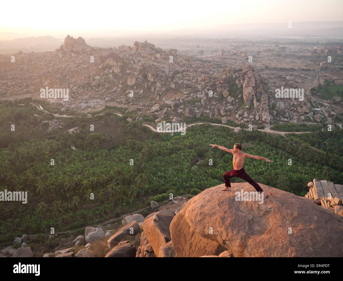 A man in yoga warrior pose in Hampi at sunrise India Stock Photo