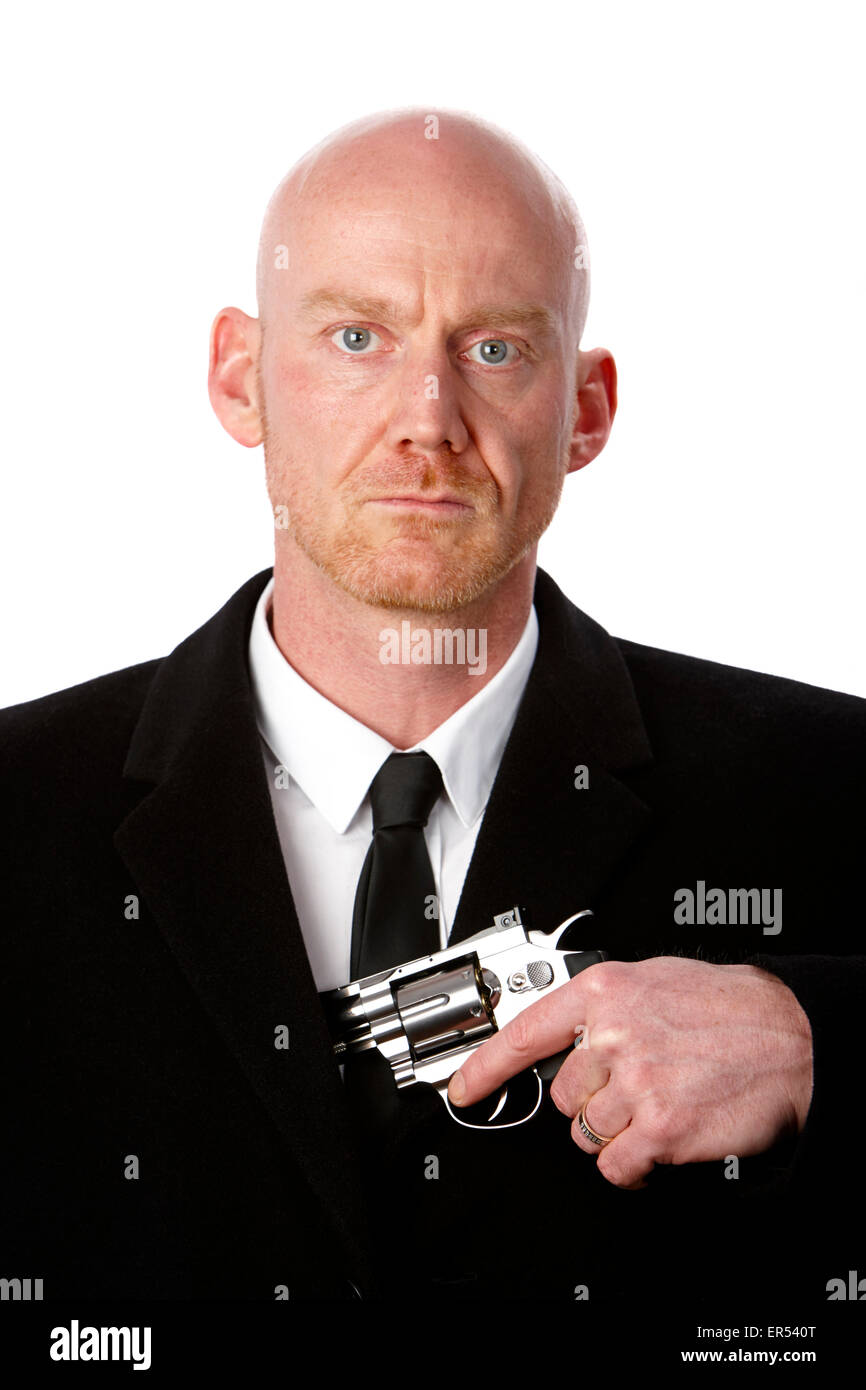 bald headed man wearing heavy black overcoat showing revolver in inside pocket against a white studio background model released Stock Photo