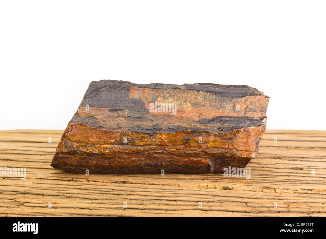 Brown piece of petrified wood on old oak surface, white background. Ancient natural gem stone. Stock Photo