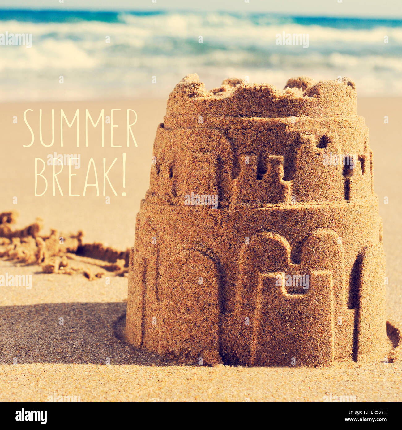 a sandcastle on the sand of a beach and the text summer break Stock Photo