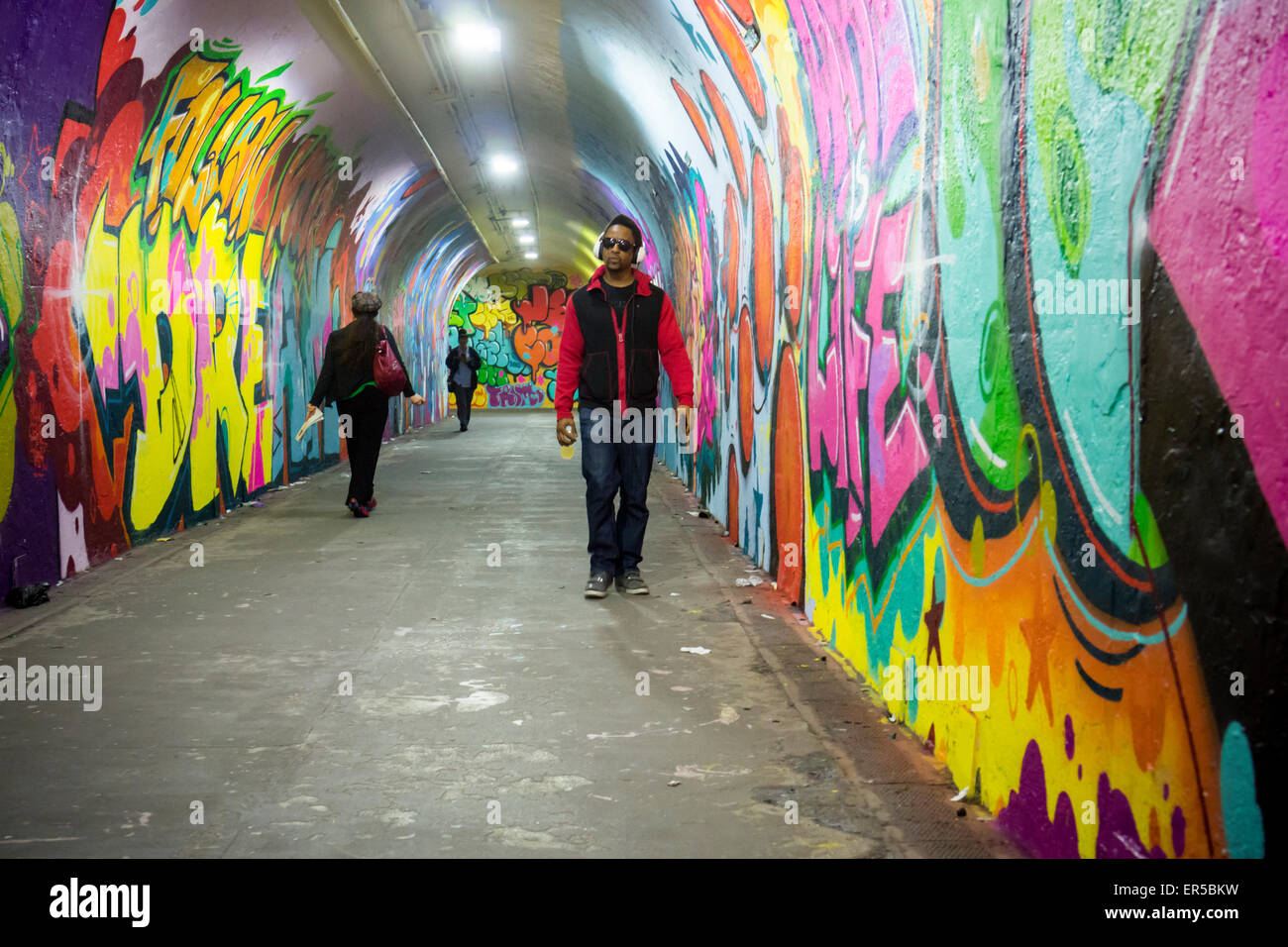 Travelers pass through the 900-foot long 191st Subway station connecting tunnel, newly decorated by artists hired by the New York City Dept. of Transportation on Thursday, May 21, 2015. The artists, COPE2, Queen Andrea, Nick Kuszyk, Cekis and Jessie Unterhalter and Katey Truhn were chosen in a competitive process by the DOT. The tunnel has recently received upgraded LED lighting and with the addition of the murals has been turned into an art gallery. (© Richard B. Levine) Stock Photo