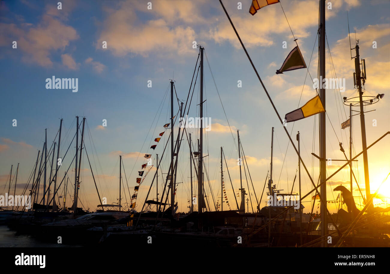 Boats with Morse flags at pier against dramatic sunset lighting (flare effect, sunset lighting) Stock Photo