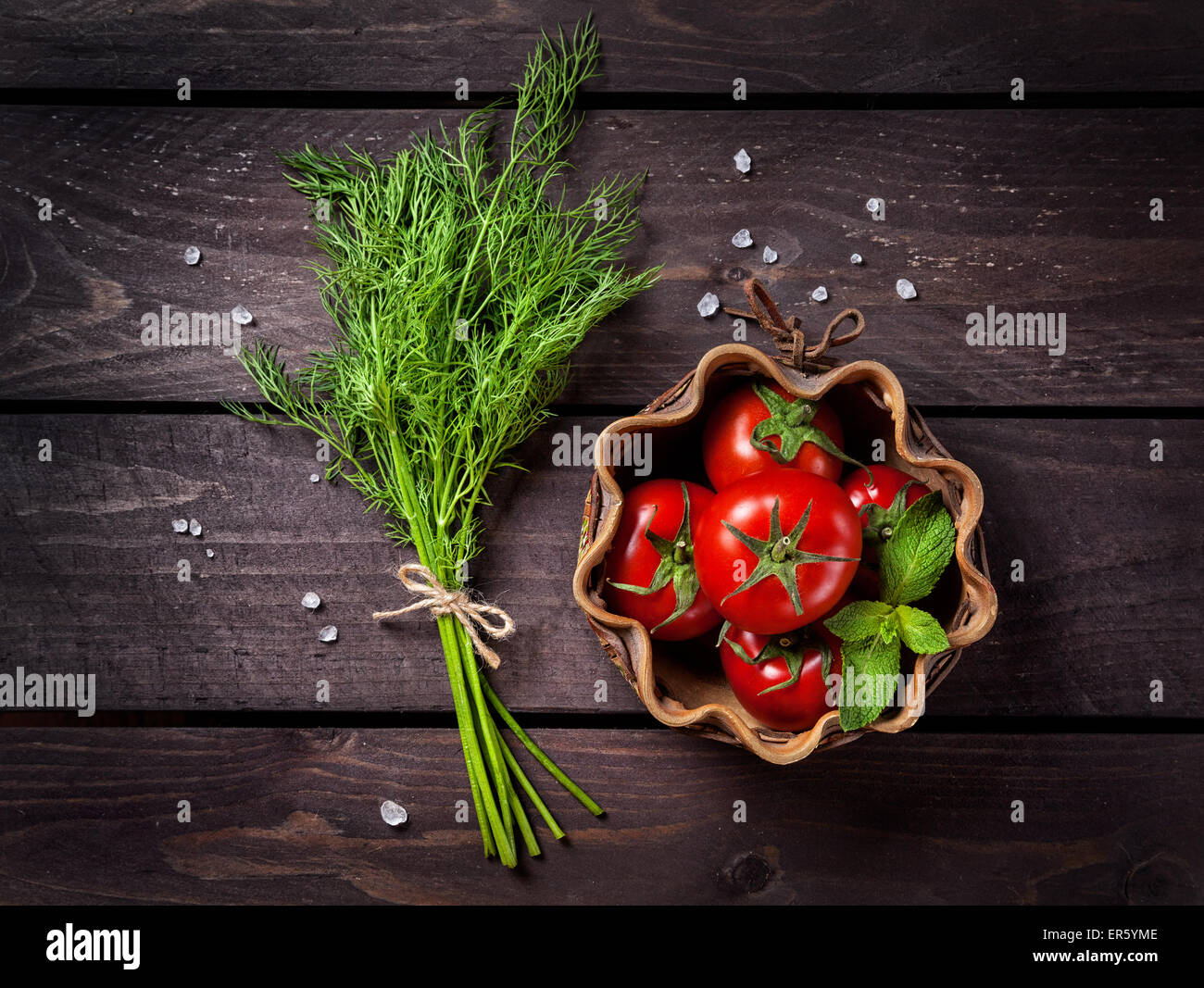 Fresh tomato, dill and mint leaves on the rustic dark wooden table in the kitchen Stock Photo