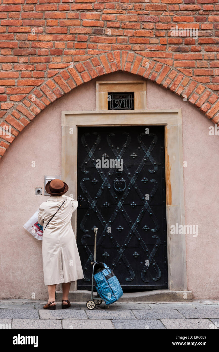 Senior Polish woman returns from shopping and stands at a metal door of a brick town home, Old Town, Warsaw, Poland, Europe Stock Photo