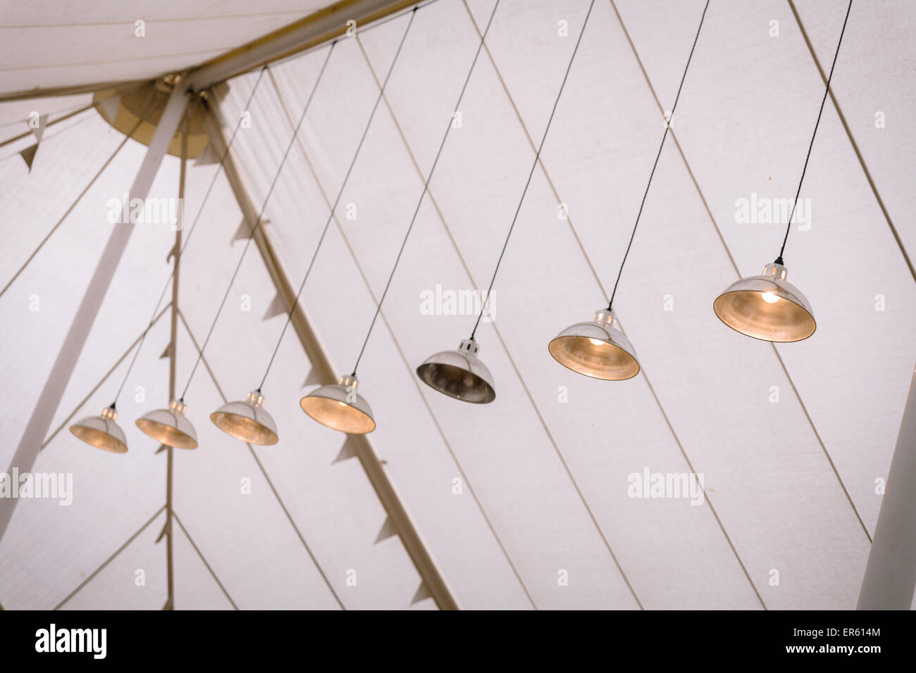 Metal lights hanging from the roof of a white marque.  One light is broken. Stock Photo