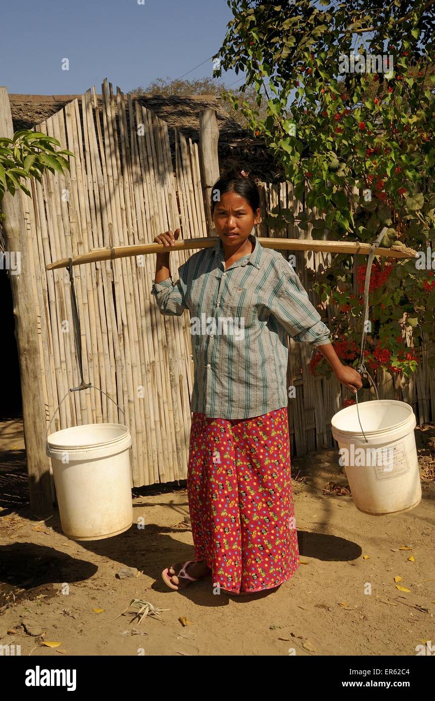 Burmese woman wearing a Longyi skirt, carrying water with a wooden pole and two buckets, Bagan, central Myanmar, Myanmar Stock Photo
