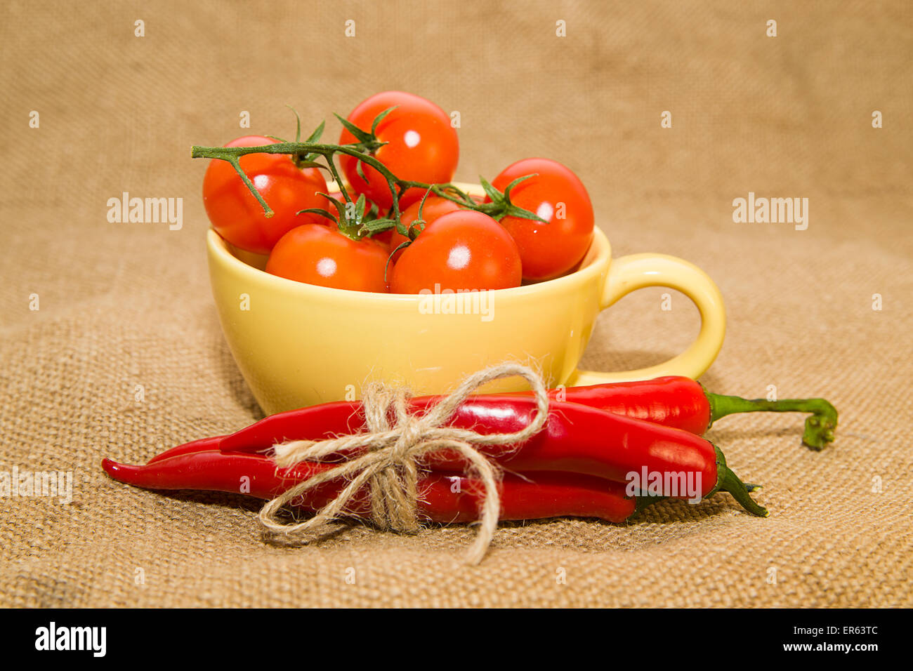 Cherry tomatoes in a yellow cup and Chile peppers tied with a rope on old cloth Stock Photo