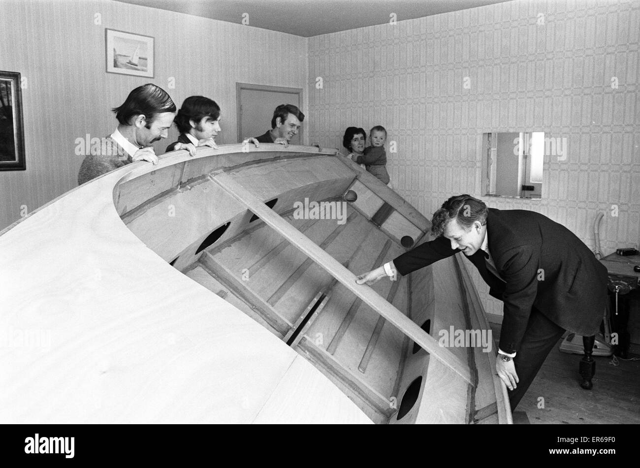 Helped by three friends and watched by his wife Betty and 20 month old son Tom, Mr Henry Fowler (right) turns the dinghy he has been building in his sitting room 11th March 1970 Stock Photo
