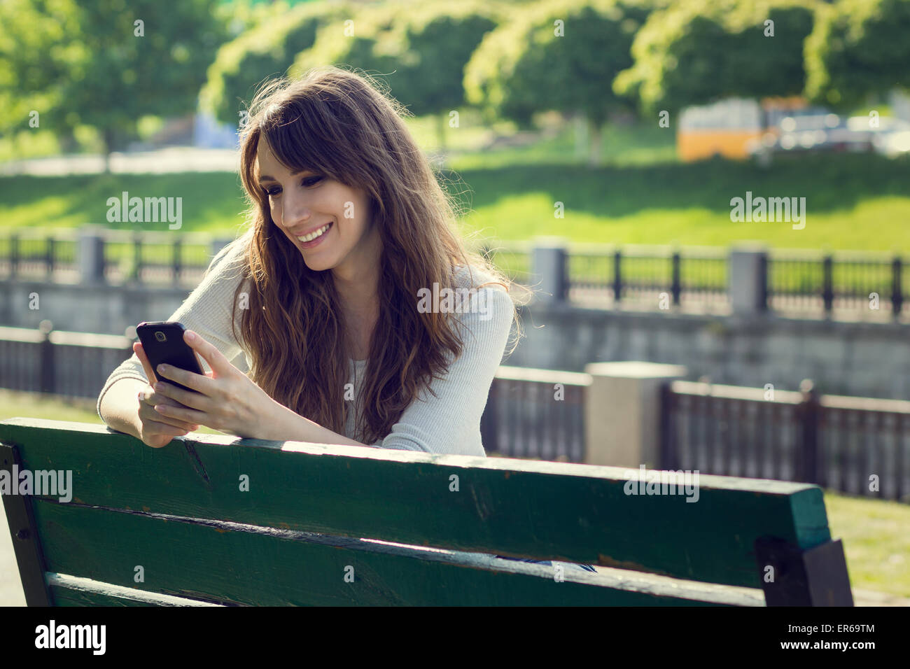 Young pretty woman chatting using phone. Smiling caucasian girl have fun with using smartphone in park Stock Photo