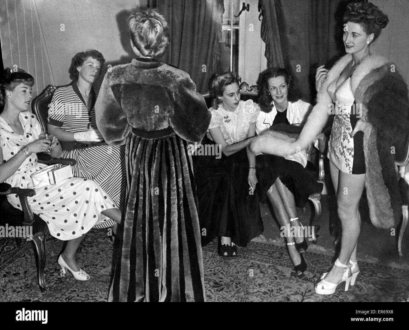 On the right mannequin Joan Sidsaph, 20, in a natural white and blue fox looks on as fashion experts study a full-length striped beaver-lamb evening coat in platinum and black (left). July 1948 P024379 Stock Photo