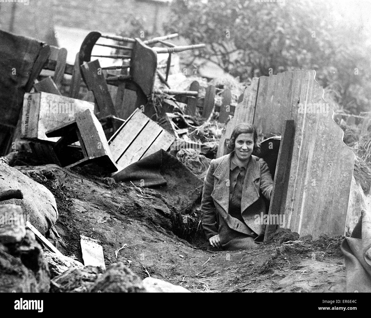A young lady emerges from an Anderson Shelter after an air raid and a heavy night of bombing. Circa: 1940 Stock Photo