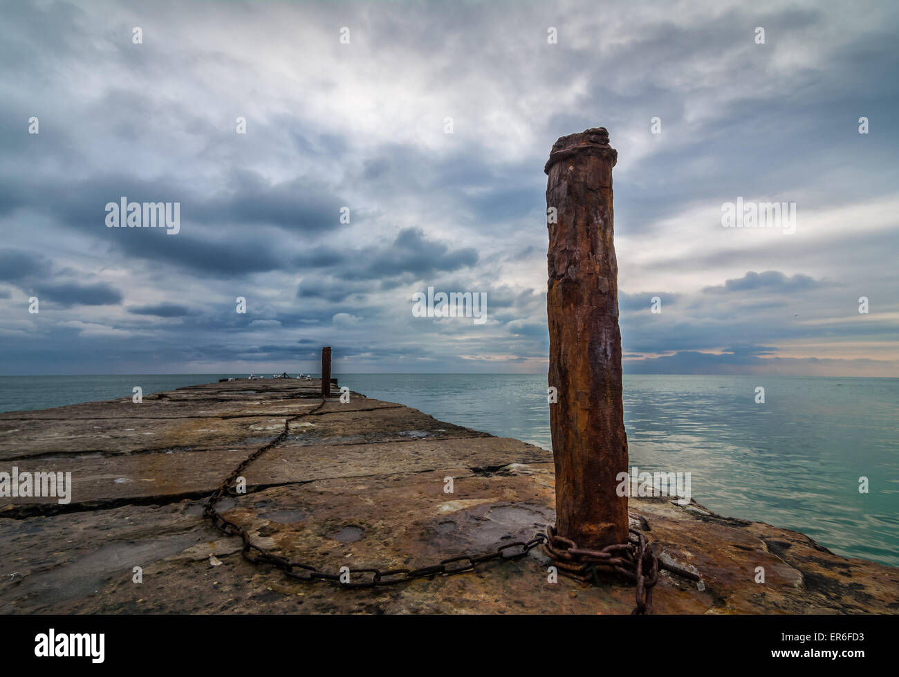 Chained together -old concrete pier with rusty chained poles Stock Photo