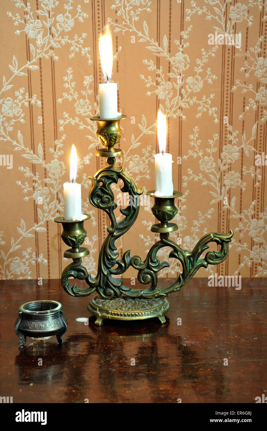 Antique candelabra with three melting candles on an old wallpaper
