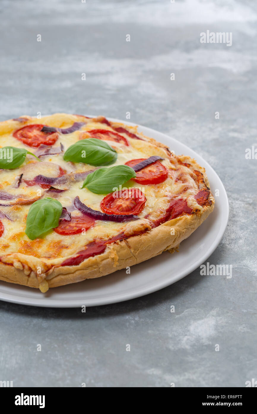 Homemade Pizza made of a flatbread with tomatoes, red onions, cheese and basil leaves on a white plate Stock Photo