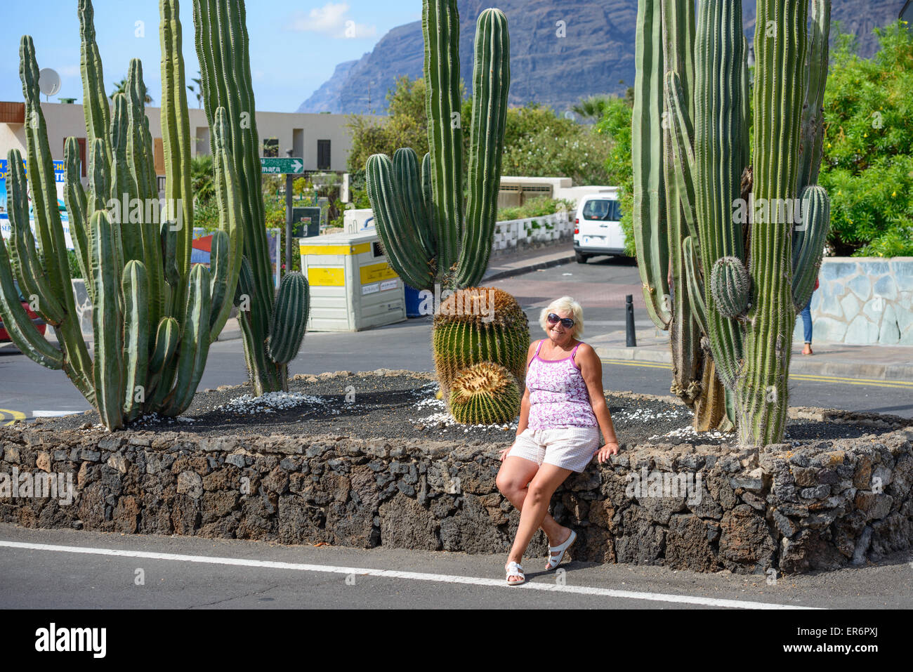 Senior lady is sitting retaining wall of cacti flower-bed on the corner of Av. Jose Gonzales Forte and Poblado Marinero and Tama Stock Photo
